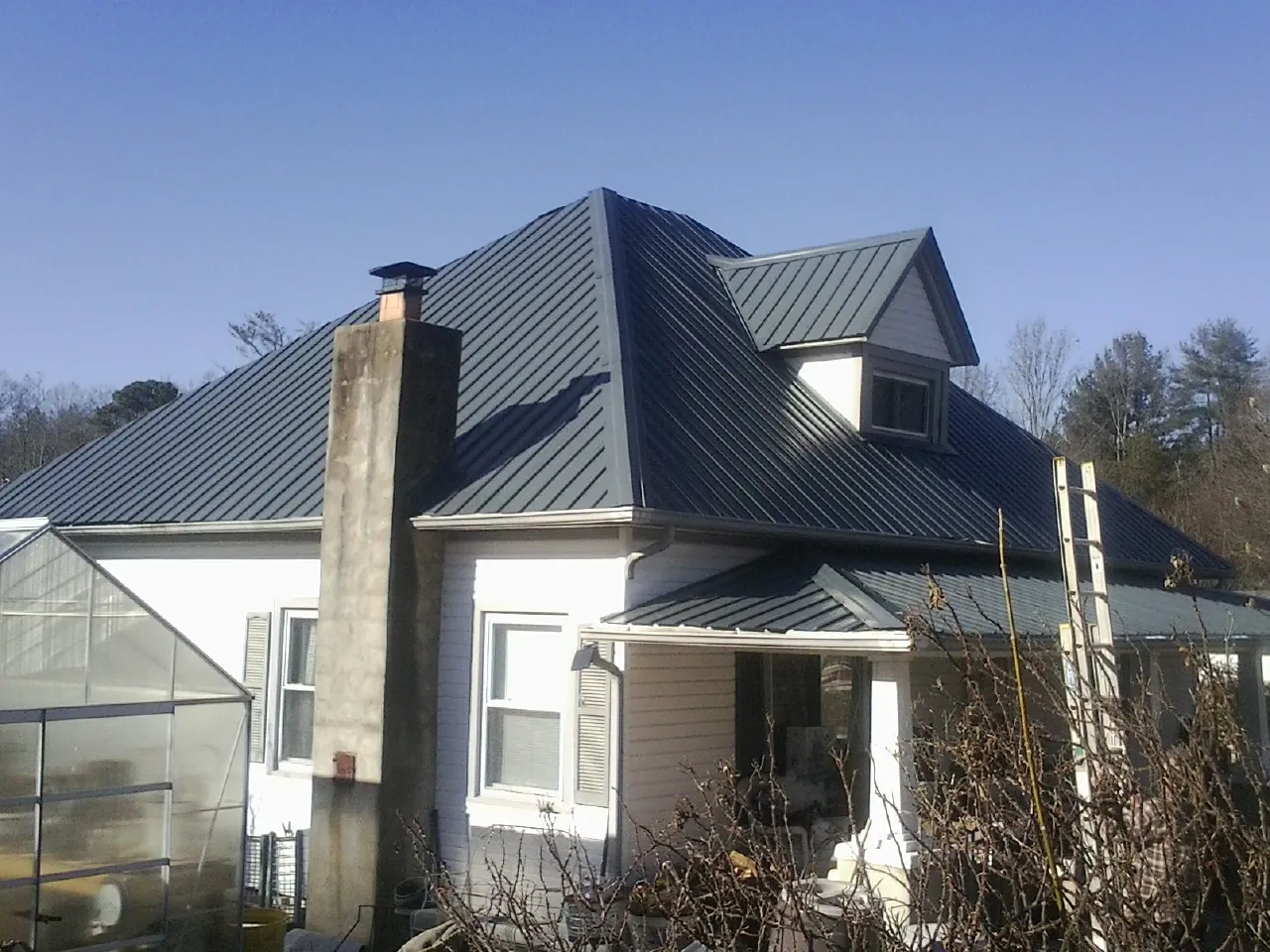 Dark blue standing seam metal roof on a white farmhouse with dormer — Slate & Tile Roof Repair by Roofing Brothers in Riverbank