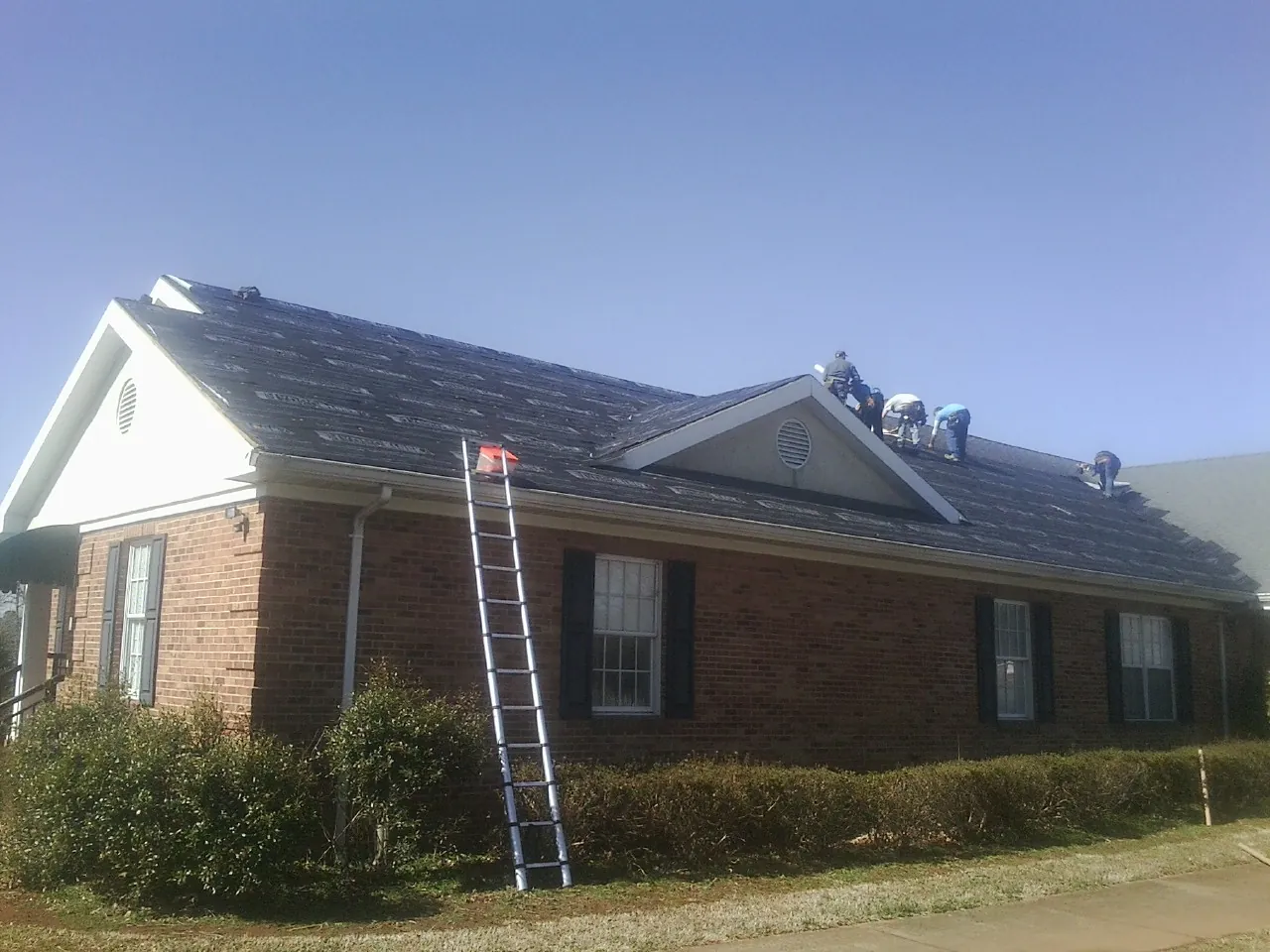 Crew tearing shingles off a brick ranch roof with a ladder set — Emergency Roof Repair work by our crew in Riverbank