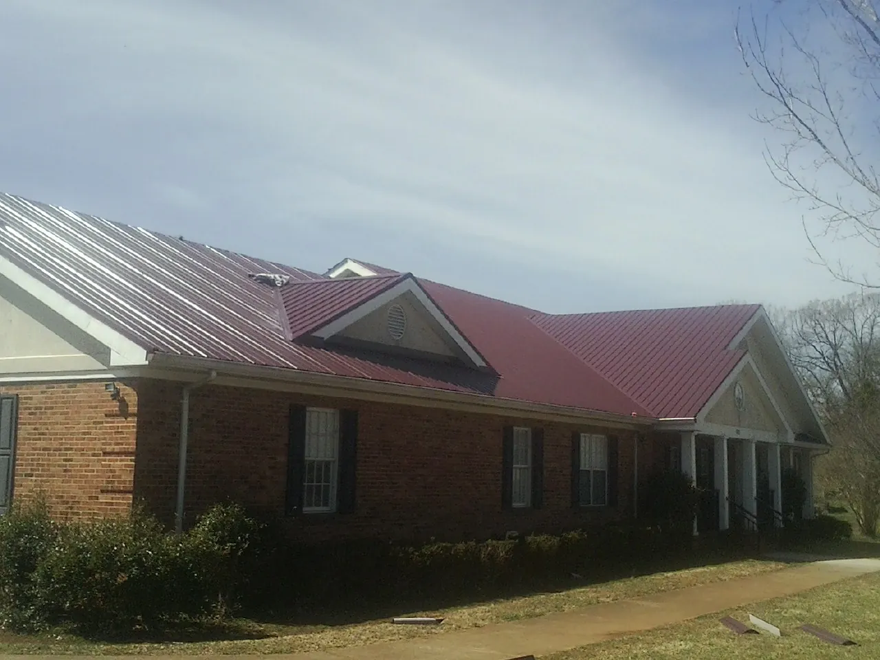 Red metal roof with gabled entries on a long brick building, from a Hail Damage Roof Repair job in Riverbank