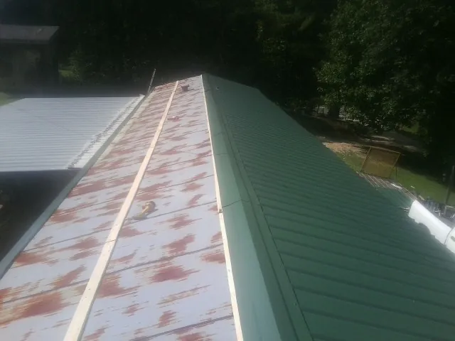 Old rusted panels beside newly installed green metal roofing — Wind Damage Roof Repair by Roofing Brothers in Riverbank
