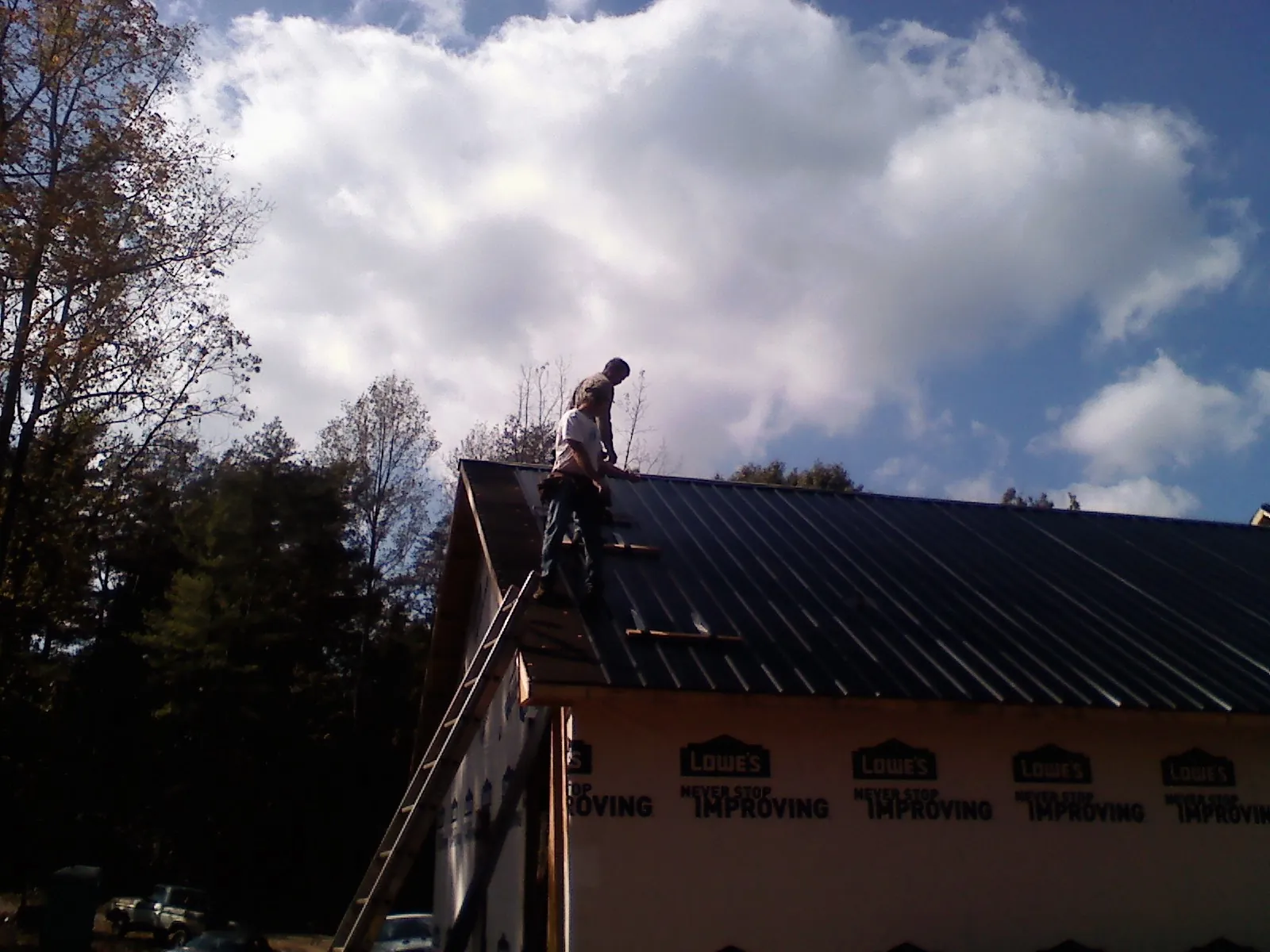 Roofer fastening dark metal panels high against a cloudy sky, from a Roof Inspection job in Riverbank