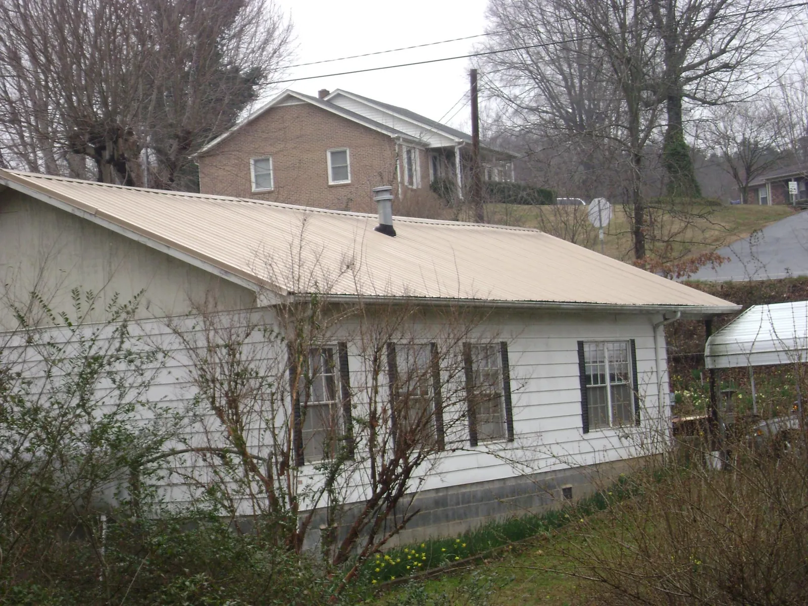 Tan metal roof on a white sided house set into a hillside — Commercial Roofing by Roofing Brothers in Riverbank
